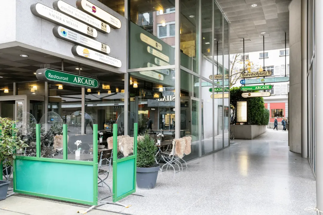 Zweiter Blick auf den Durchgang zum Eingang der BANK-now Filiale Baden mit Schildern.