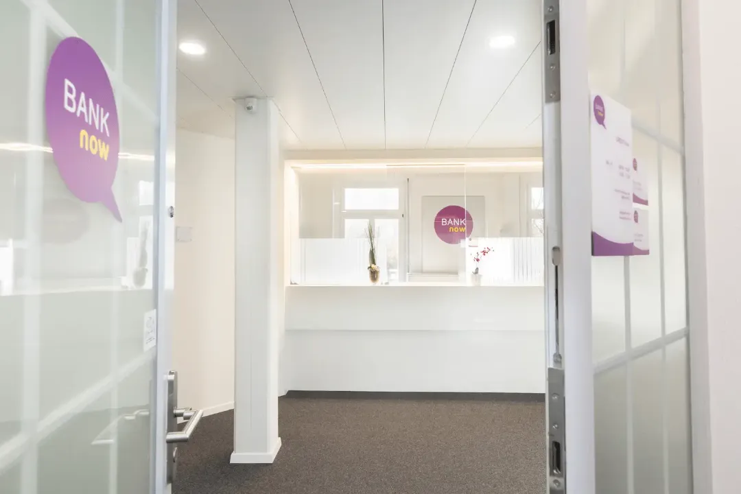 Heller Schalterbereich der BANK-now Filiale Luzern mit Empfangstheke und Glaswand.