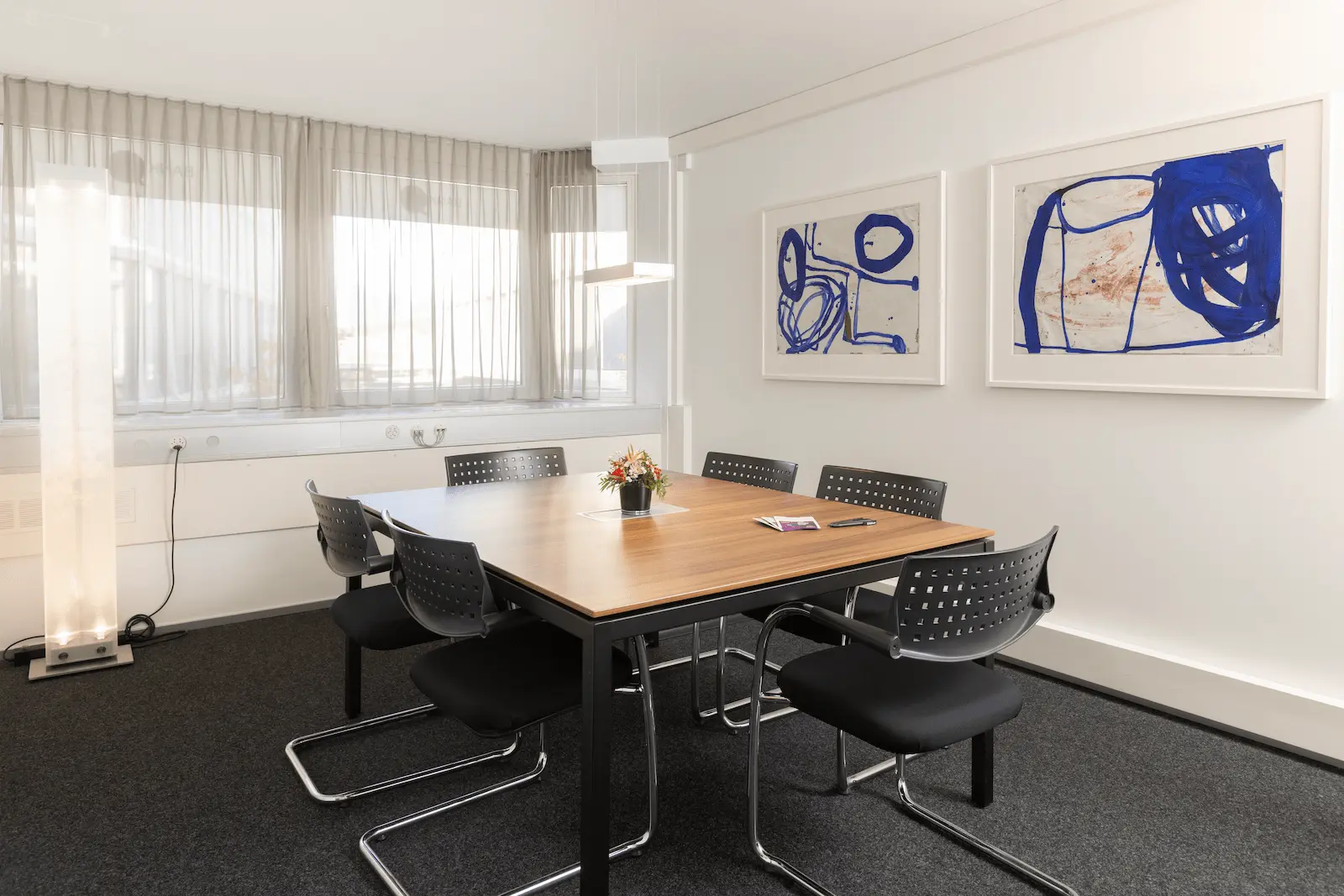 Besprechungsraum der BANK-now Filiale Chur mit grossem Tisch, mehreren Stühlen und Wandbildern.